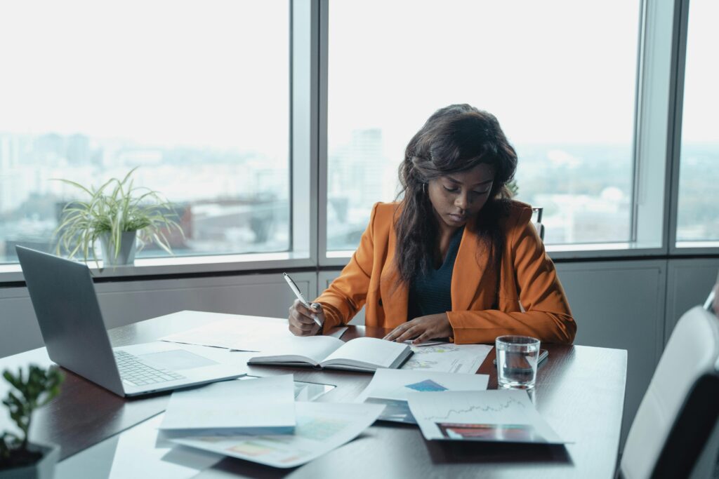 Focused black businesswoman analyzing documents at an office desk with city view.